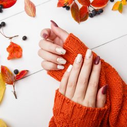 deux bras avec un pull orange des ongles colorés et des feuilles d'automne