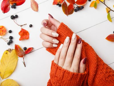 deux bras avec un pull orange des ongles colorés et des feuilles d'automne