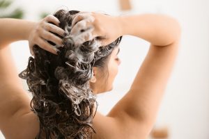 femme de dos dans une douche qui se lave les cheveux avec du shampooing